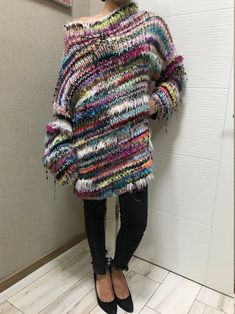 a woman standing next to a wall wearing a multicolored sweater