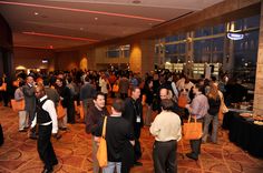 a large group of people standing in a room with many bags on the floor and tables full of food