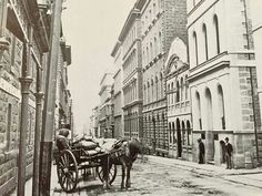 an old black and white photo of two horses pulling a carriage down a narrow street