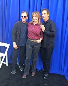 three people standing next to each other in front of a blue curtain and white chair