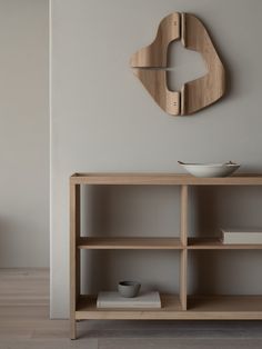 a wooden shelf sitting next to a white bowl on top of a table in front of a clock