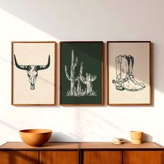 three framed pictures hang on the wall next to a bowl and wooden cabinet in a room