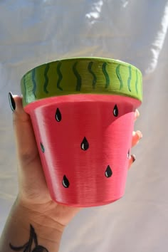 a hand holding a cup with watermelon painted on the side and black dots