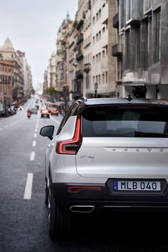 the back end of a silver minivan driving down a city street with buildings on both sides