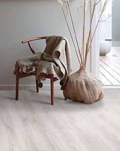 a chair sitting next to a vase with dry grass in it and a blanket on the back