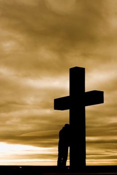 a person standing in front of a cross on top of a hill with clouds behind them