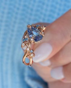 a woman's hand holding a gold ring with blue and white stones on it