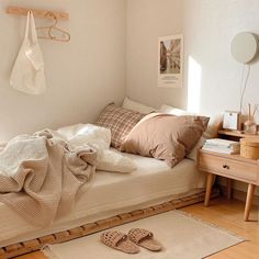 an unmade bed in a small room with wooden floors and white walls, along with various items on the floor