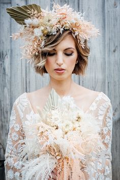 a woman with flowers in her hair wearing a white lace dress and holding a bouquet