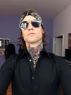 a man with tattoos wearing sunglasses and a bandanna around his neck is looking at the camera