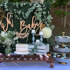 a dessert table with cupcakes, cake and greenery on the top shelf