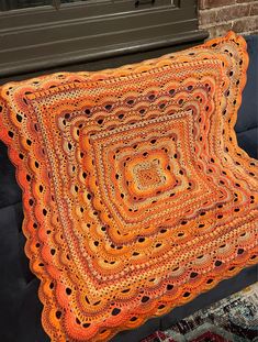 an orange crocheted blanket sitting on top of a black bench next to a window