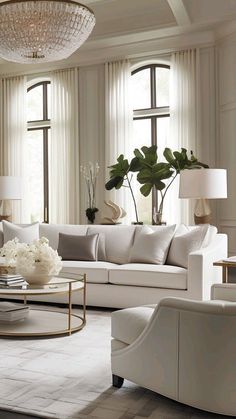 a living room filled with white furniture and lots of window sill space next to a chandelier