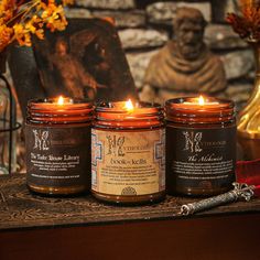 three candles sitting on top of a table next to a vase with flowers and a statue in the background