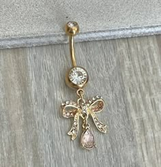 a gold colored belly ring with an angel design and crystal stones on the bottom, attached to a wall