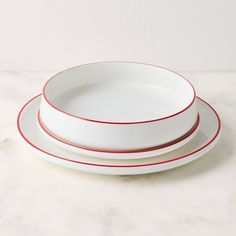 three white plates with red lines on them sitting on a marble counter top, one is empty