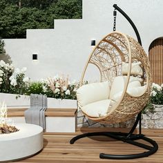 a hanging egg chair next to a fire pit on a wooden deck with white flowers in the background