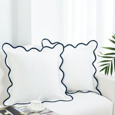 two pillows sitting on top of a white couch next to a potted palm tree