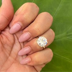 a woman's hand holding a ring with a diamond on it and green leaves in the background