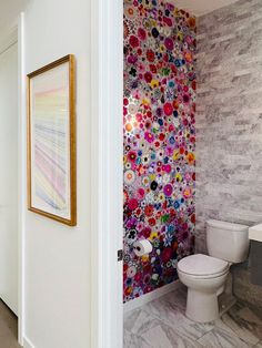 a bathroom with a white toilet sitting next to a wall covered in colorful flowers on it