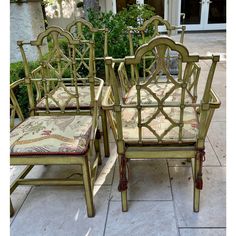 four green bamboo chairs sitting next to each other on a sidewalk with plants in the background