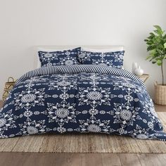 a bed with blue and white flowers on it in a room next to a potted plant