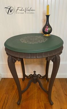 a green table with a black vase on top and a candle in the corner next to it