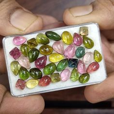 a person holding a small box filled with lots of different colored stones in their hands