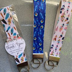 three pairs of blue, pink and yellow feather print lanyards with thank you tags on them