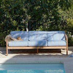 a blue and white striped couch next to a swimming pool with trees in the background