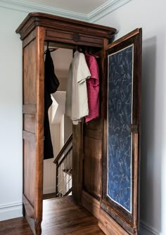 an open wooden cabinet with clothes hanging on it