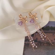 Gorgeous purple lily flower and gold bow layering tassel dangly statement earrings. Adorable lilac bohemian floral charm combined with delicate gold bow, with double pearl beads and double gold chains dangles. Super cute dainty feminine earrings, absolutely unique and eye catching! 💎 Features: ♥ Handcrafted Jewelry ♥ Material: Finest 14K Gold plated ♥ Main stone: Resin ♥ Side Stone: cultured pearl ♥ Approximate Measurements: - Length: 3.2" - Width: 0.8" ♥ Lightweight, easy to wear ♥ Nickel/Lead Purple Lily Flower, Purple Statement Earrings, Tulip Earrings, Purple Lily, Feminine Earrings, Flower Earrings Gold, Tassel Earing, Chain Drop Earrings, Romantic Earrings