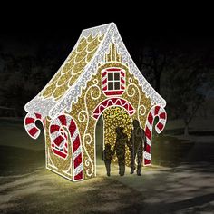 two people standing in front of a lit up gingerbread house