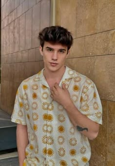 a young man standing next to a wall with his hand in his pocket and looking at the camera