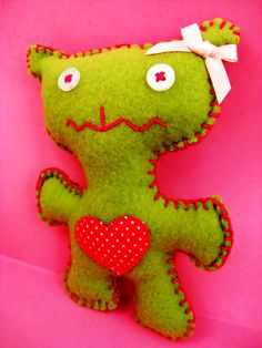 a green teddy bear with a red heart on it's chest sitting against a pink background