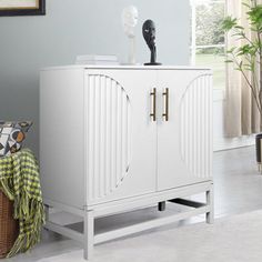 a white cabinet sitting on top of a floor next to a potted plant in a living room