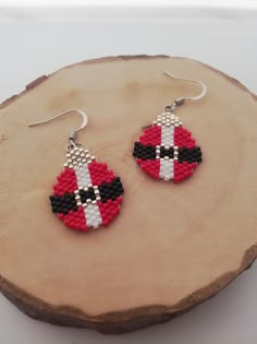 a pair of red and black beaded earrings sitting on top of a piece of wood