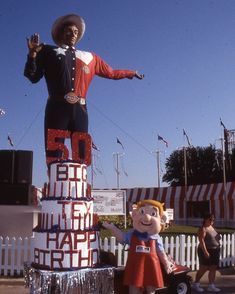 a giant statue of a man standing on top of a birthday cake in front of a fence