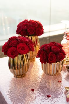 three gold vases filled with red roses on a table