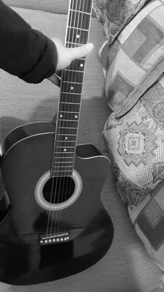 a black and white photo of someone playing an acoustic guitar on a couch with a pillow in the background