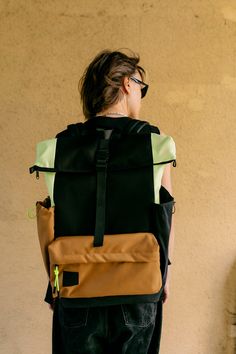 a person with a backpack on their back standing in front of a wall and wearing sunglasses