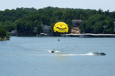 a yellow smiley face balloon being pulled by a boat in the water with a wake board