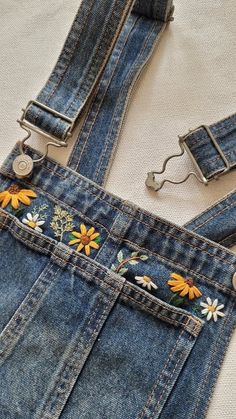 a pair of jean overalls with sunflower embroidered on the front and back straps