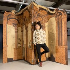 a woman standing in front of a wooden room divider with intricate carvings on it