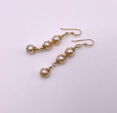 Unique presentation of peach freshwater pearls, antique gold spacers, and filigree bead caps in these elegant dangle earrings. The dangles are connected to each other and to the gold filled earwire through gold filled wrapped loops.  The earrings are about 1 1/4 inches long, measured from the earwire, and come nestled comfortably on a bed of cotton in a white cardboard box. Made in the USA by me. NA-821-0624-1111 Gold Beaded Pearl Earrings, Gold Pearl Earrings With Gold Beads, Gold Earrings With Pearl Drop, Gold Earrings With Pearl Drop And Round Beads, Elegant Gold Pearl Earrings With Gold Beads, Gold Pearl Drop Beaded Earrings, Gold Beaded Dangle Earrings With Pearl Drop, Gold Dangle Beaded Earrings With Pearl Drop, Gold Pearl Earrings With Round Beads