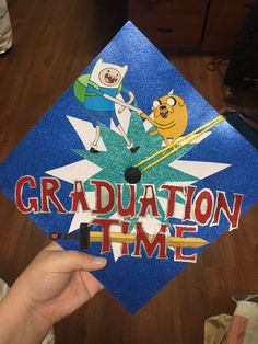 a person holding up a graduation cap with cartoon characters on it and the words graduation time