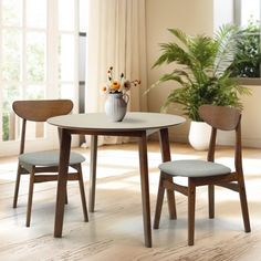 two chairs and a table in a room with plants on the windowsills behind them