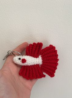 a hand holding a red and white crocheted keychain with a fish on it