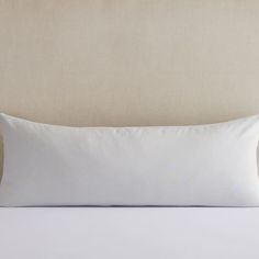 a white pillow sitting on top of a bed next to a beige headboard and pillows