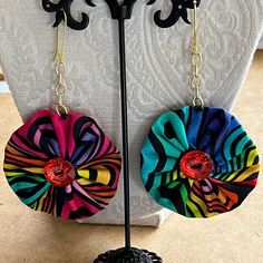 a pair of colorful flower shaped earrings hanging from a black metal hook on a stand